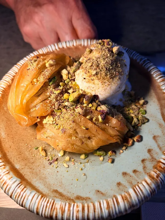 Dessert van filodeeg met pistache en een bol room op een aardewerk bord