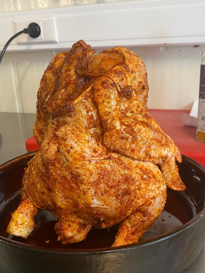 Een hele gekruide kip rechtop in de kamado